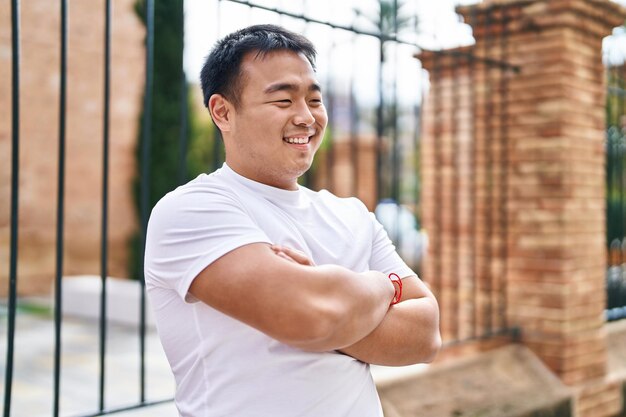 Junger chinesischer Mann lächelt selbstbewusst mit verschränkten Armen auf der Straße