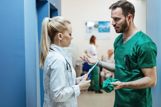 Junger Chirurg und Ärztin kommunizieren, während sie in einer Lobby einer Klinik stehen