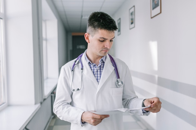 Junger Doktor mit den Papieren, die in der Klinik stehen