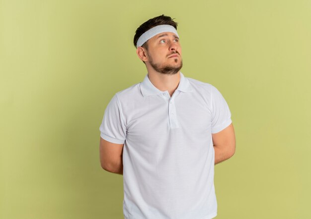 Junger Eignungsmann im weißen Hemd mit dem Stirnband, das beiseite schaut verwirrt über Olivenhintergrund schaut