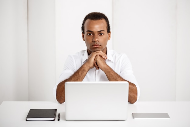 Kostenloses Foto junger erfolgreicher geschäftsmann, der am arbeitsplatz mit laptop sitzt
