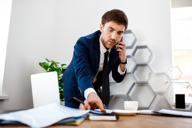 Junger erfolgreicher Geschäftsmann, der am Telefon, Bürohintergrund spricht.