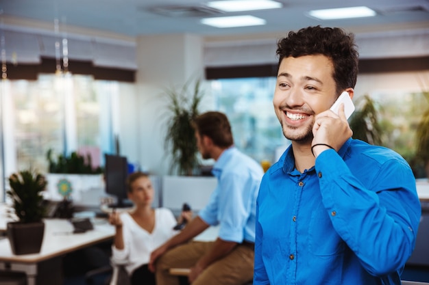 Junger erfolgreicher Geschäftsmann, der am Telefon, lächelnd, über Büro spricht