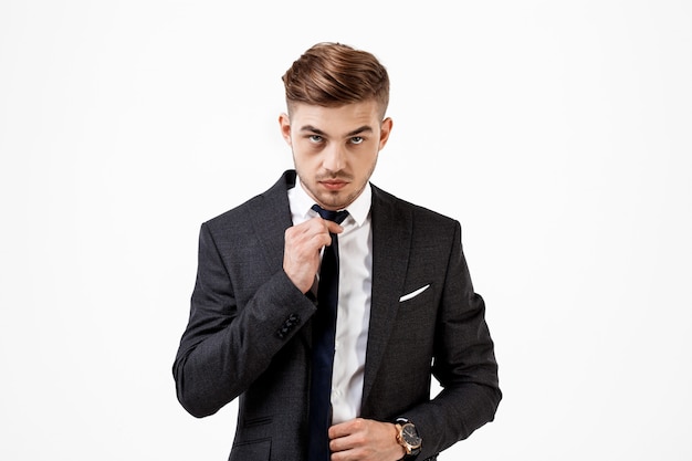 Junger erfolgreicher Geschäftsmann im Anzug, der Krawatte korrigiert.