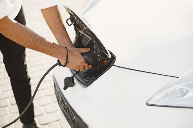 Junger erwachsener Mann, der sein Elektroauto in der Stadt auflädt. Öko-Elektroauto-Konzept.