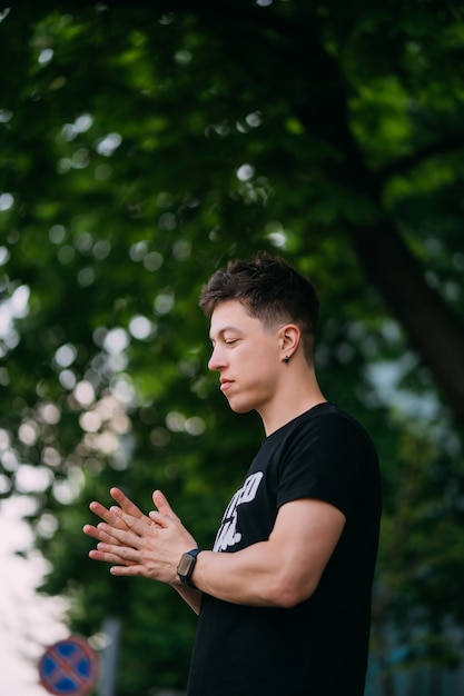 Junger erwachsener Mann in einem schwarzen T-Shirt und in Jeans geht auf einer Stadtstraße an einem sonnigen Tag