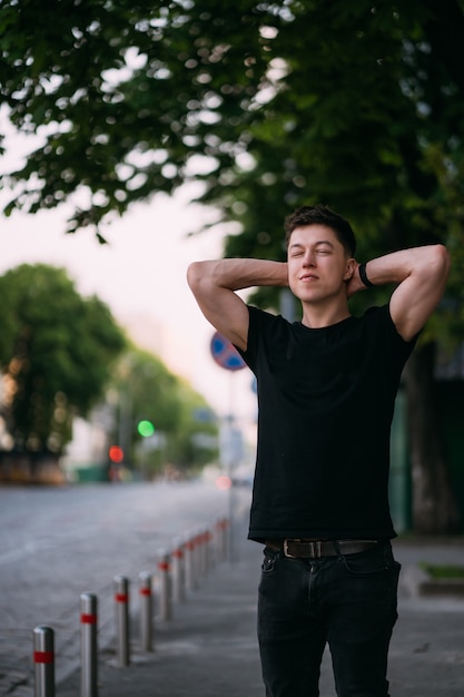 Junger erwachsener Mann in einem schwarzen T-Shirt und in Jeans geht auf einer Stadtstraße