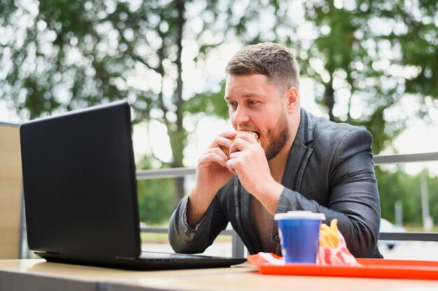 Junger essender Mann beim Betrachten des Laptops