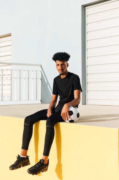 Junger ethnischer Mann, der mit Fußball sitzt