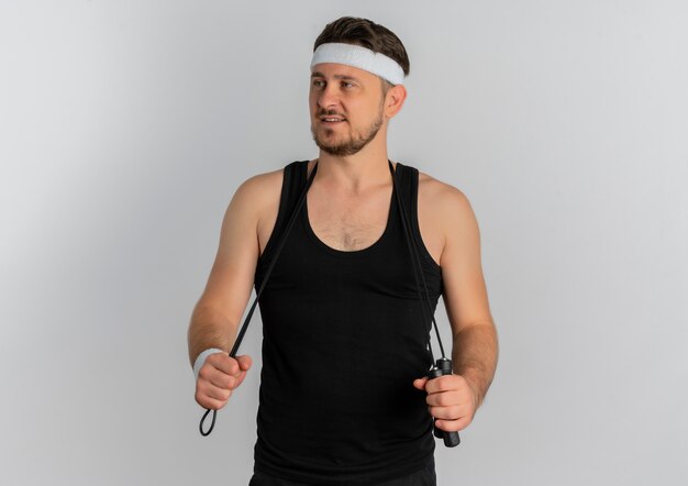 Junger Fitness-Mann mit dem Stirnband, das das Überspringen schaut, das sicher steht, über weißem Hintergrund zu stehen