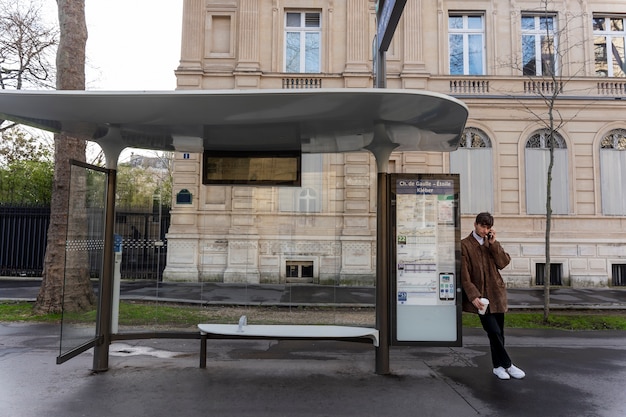 Junger Franzose, der am Bahnhof auf den Bus wartet und auf dem Smartphone spricht