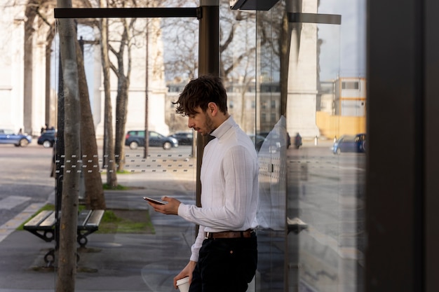 Junger Franzose wartet am Bahnhof auf den Bus und benutzt sein Smartphone