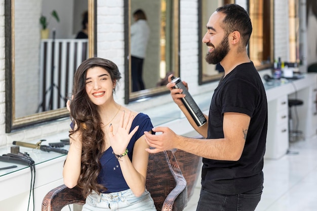 Junger Friseur mit Spray und seinem Kunden, der mit ihm lacht