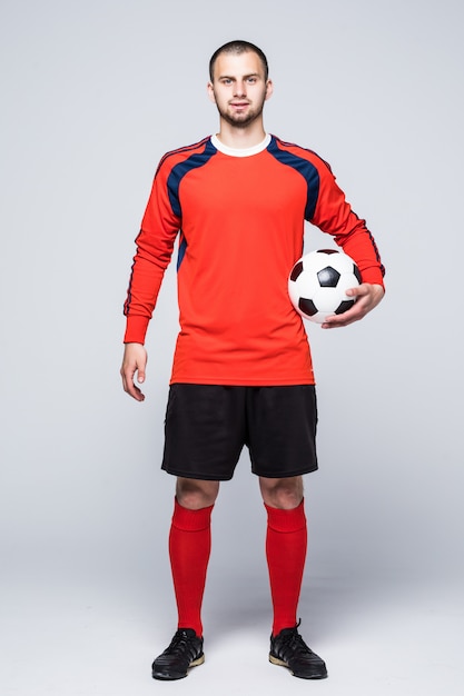 Kostenloses Foto junger fußballspieler mit ball unter der hand gekleidet im roten trikot vor weiß
