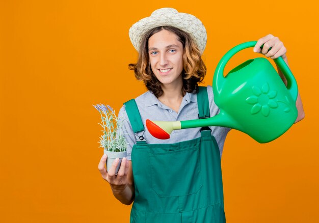 Junger Gärtnermann, der Overall und Hut hält Bewässerungsdose trägt