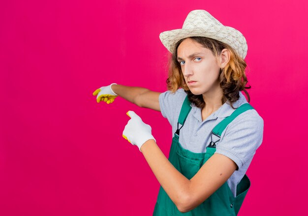 Junger Gärtnermann, der Overall und Hut trägt Gummihandschuhe trägt