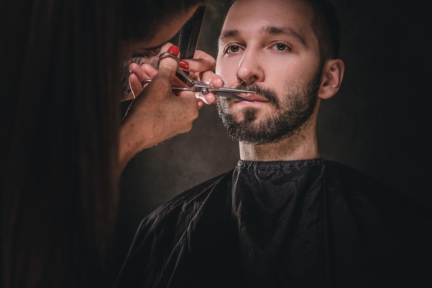 Junger Gentleman genießt Schnurrbart- und Barttrimmen im dunklen Friseursalon.