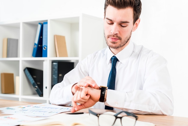 Junger Geschäftsmann am Arbeitsplatz die Zeit auf Armbanduhr aufpassend