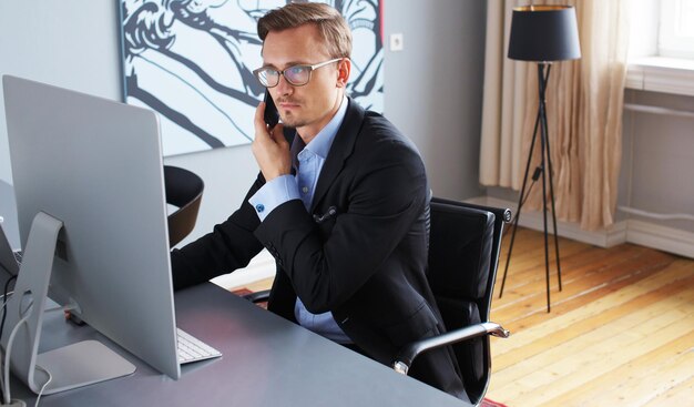 Junger Geschäftsmann, der am Telefon im Büro spricht.