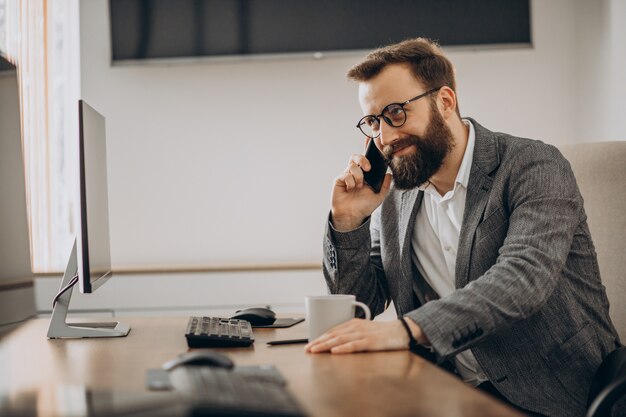 Junger Geschäftsmann, der am Telefon spricht und am Computer arbeitet