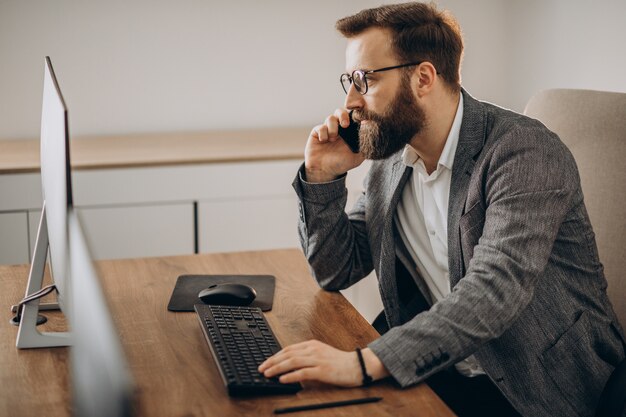 Junger Geschäftsmann, der am Telefon spricht und am Computer arbeitet