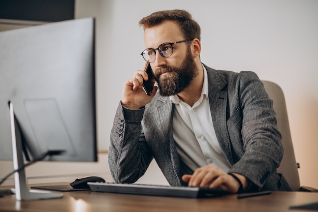 Junger Geschäftsmann, der am Telefon spricht und am Computer arbeitet