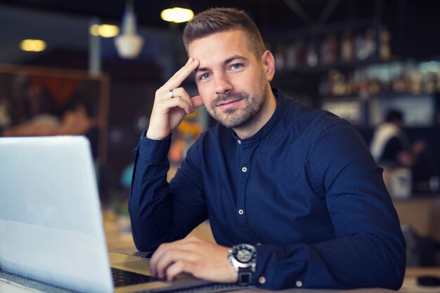 Junger Geschäftsmann, der an der Cafeteria mit Laptop-Computer auf dem Tisch sitzt