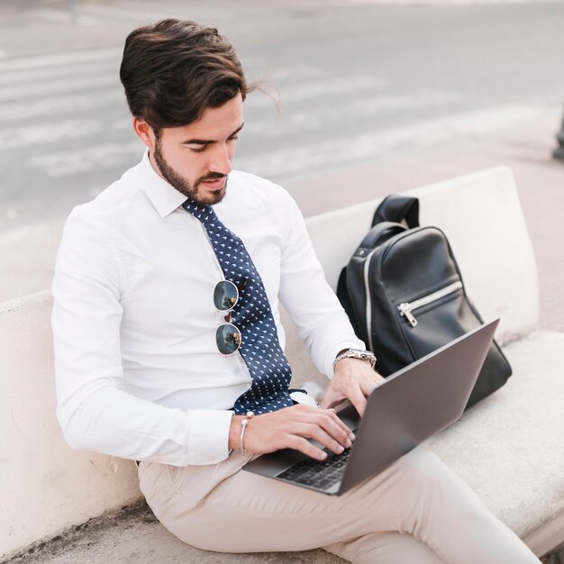 Junger Geschäftsmann, der auf der Bank arbeitet an Laptop sitzt