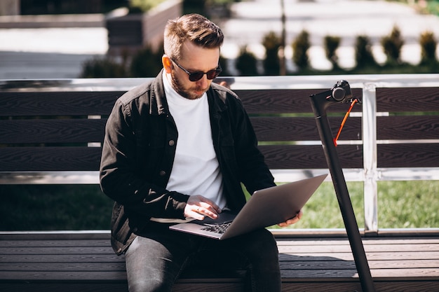 Junger Geschäftsmann, der auf der Bank sitzt und am Computer arbeitet