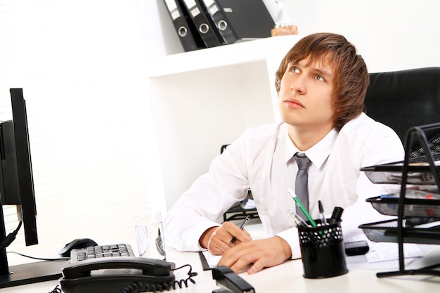 Junger Geschäftsmann, der im Büro denkt