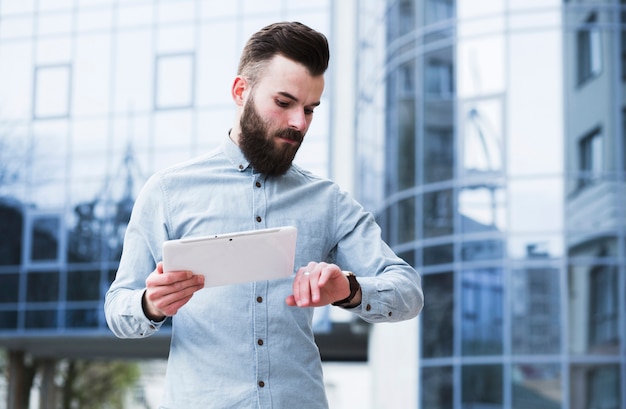 Kostenloses Foto junger geschäftsmann, der in der hand die digitale tablette überprüft zeit hält