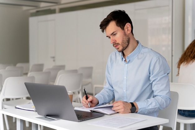 Junger Geschäftsmann, der mit Laptop an ihrem Schreibtisch arbeitet