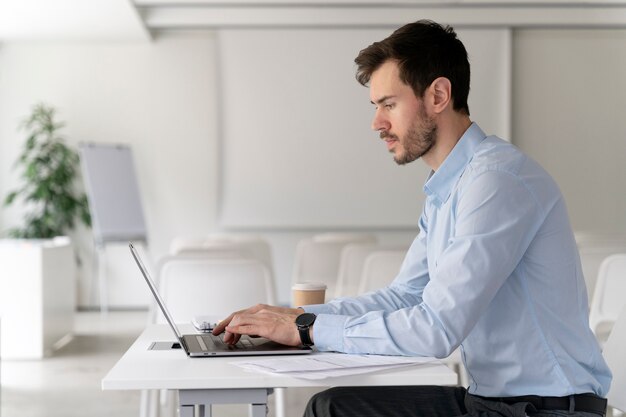 Junger Geschäftsmann, der mit Laptop an ihrem Schreibtisch arbeitet