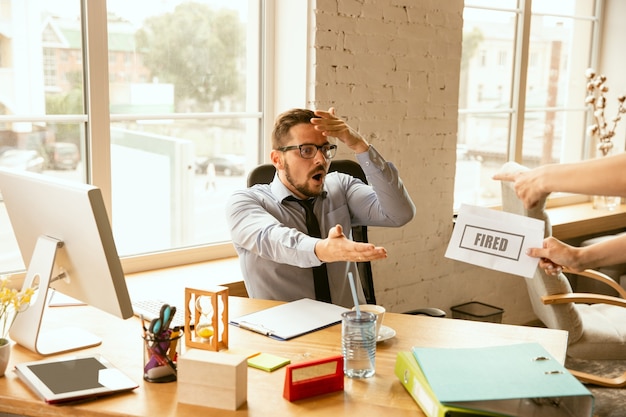 Kostenloses Foto junger geschäftsmann gefeuert, sieht verärgert aus. muss seine bürogegenstände packen und den arbeitsplatz für neue arbeiter verlassen. probleme in beruf, stress, arbeitslosigkeit, neuer lebensweise oder karriereende.