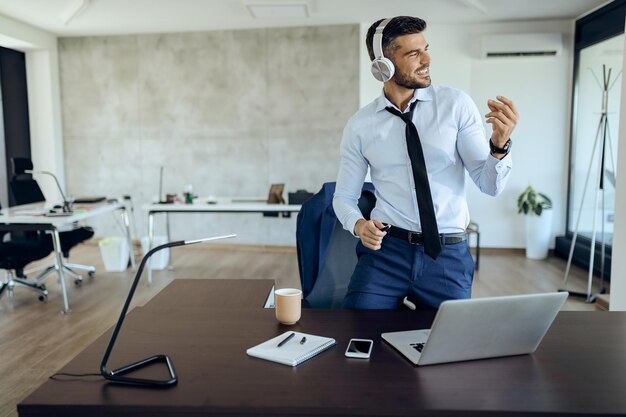 Junger Geschäftsmann hat Spaß beim Hören von Musik über Kopfhörer im Büro