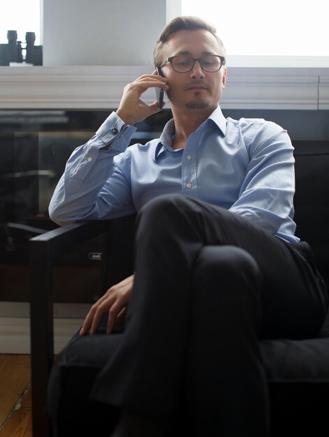 Junger Geschäftsmann in dunkelblauer Anzughose und in einem blauen Hemd, das mit Handy im Büro kühlt.