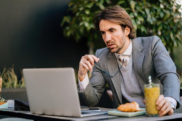 Junger Geschäftsmann liest eine E-Mail auf dem Laptop, während er in einem Café sitzt