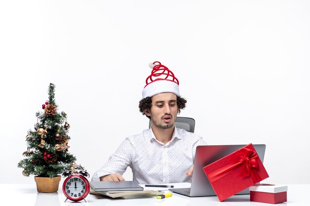 Junger Geschäftsmann mit lustigem Weihnachtsmannhut, der Weihnachten im Büro feiert