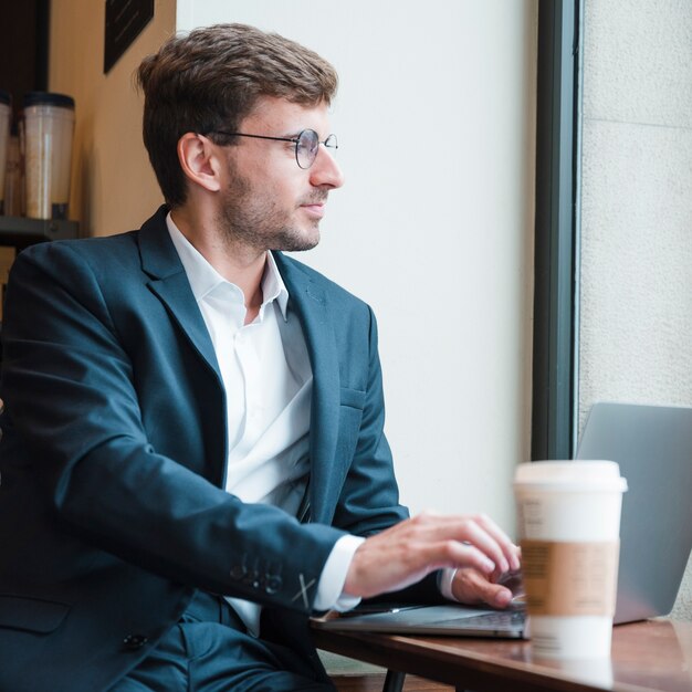 Junger Geschäftsmann unter Verwendung des Laptops im Café, das weg schaut