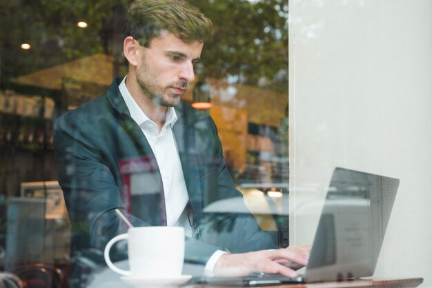 Junger Geschäftsmann unter Verwendung des Laptops mit Tasse Kaffee im Café