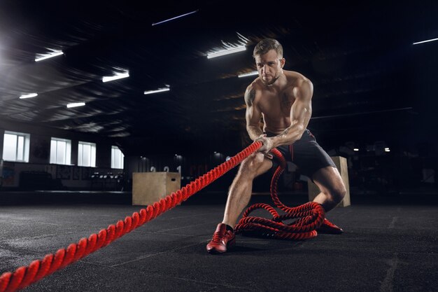 Junger gesunder Mann, Athlet, der Übung mit den Seilen im Fitnessstudio tut