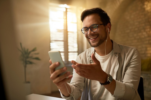 Junger glücklicher Geschäftsmann, der Handy verwendet, während er im Büro arbeitet