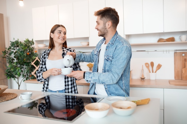 Junger glücklicher Mann und Frau in der Küche, Frühstück, Paar zusammen am Morgen, lächelnd, Tee trinkend