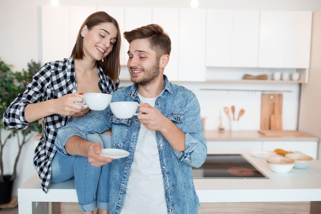 Junger glücklicher Mann und Frau in der Küche, Frühstück, Paar zusammen am Morgen, lächelnd, Tee trinkend