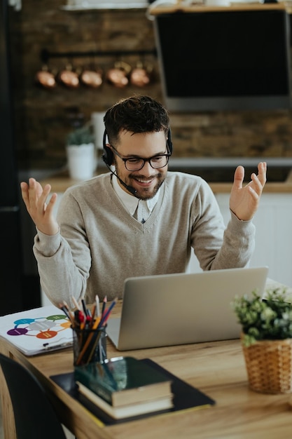 Junger glücklicher Unternehmer, der zu Hause einen Videoanruf über einen Computer hat