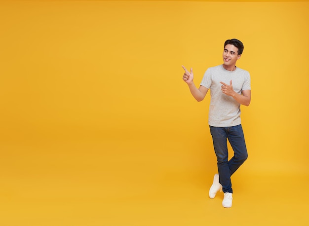 Junger gutaussehender asiatischer Mann, der mit dem Finger in den leeren Raum zeigt, auf isoliertem gelbem Studiohintergrund