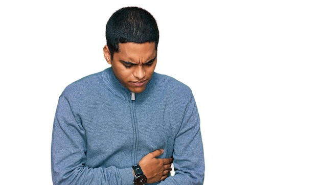 Kostenloses Foto junger gutaussehender hispanischer mann trägt lässiges sweatshirt mit der hand auf dem bauch, weil er verdauungsstörungen und eine schmerzhafte krankheit hat und sich unwohl fühlt. schmerzkonzept.
