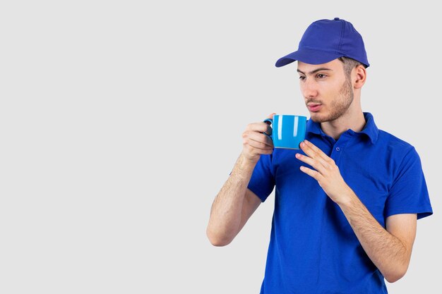 Junger gutaussehender junge in blauer uniform, der eine tasse tee trinkt