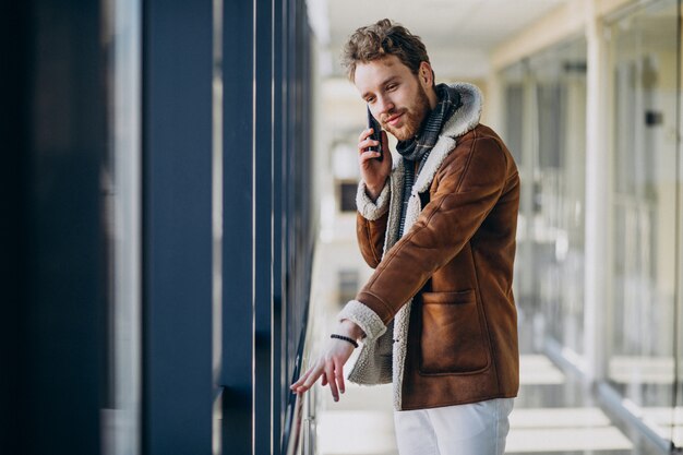 Junger gutaussehender Mann am Flughafen sprechend am Telefon