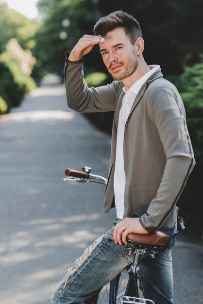 Junger gutaussehender Mann auf dem Fahrrad, das Auge abschirmt